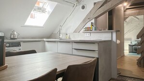 Une cuisine moderne dotée d’une verrière, un coin repas avec une table en bois et un escalier menant à l’étage supérieur.