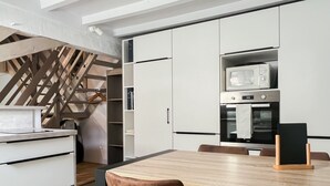 Une cuisine moderne avec des meubles blancs, un four à micro-ondes encastré et un four double. On y trouve une table à manger avec des chaises et un mur décoratif en bois.