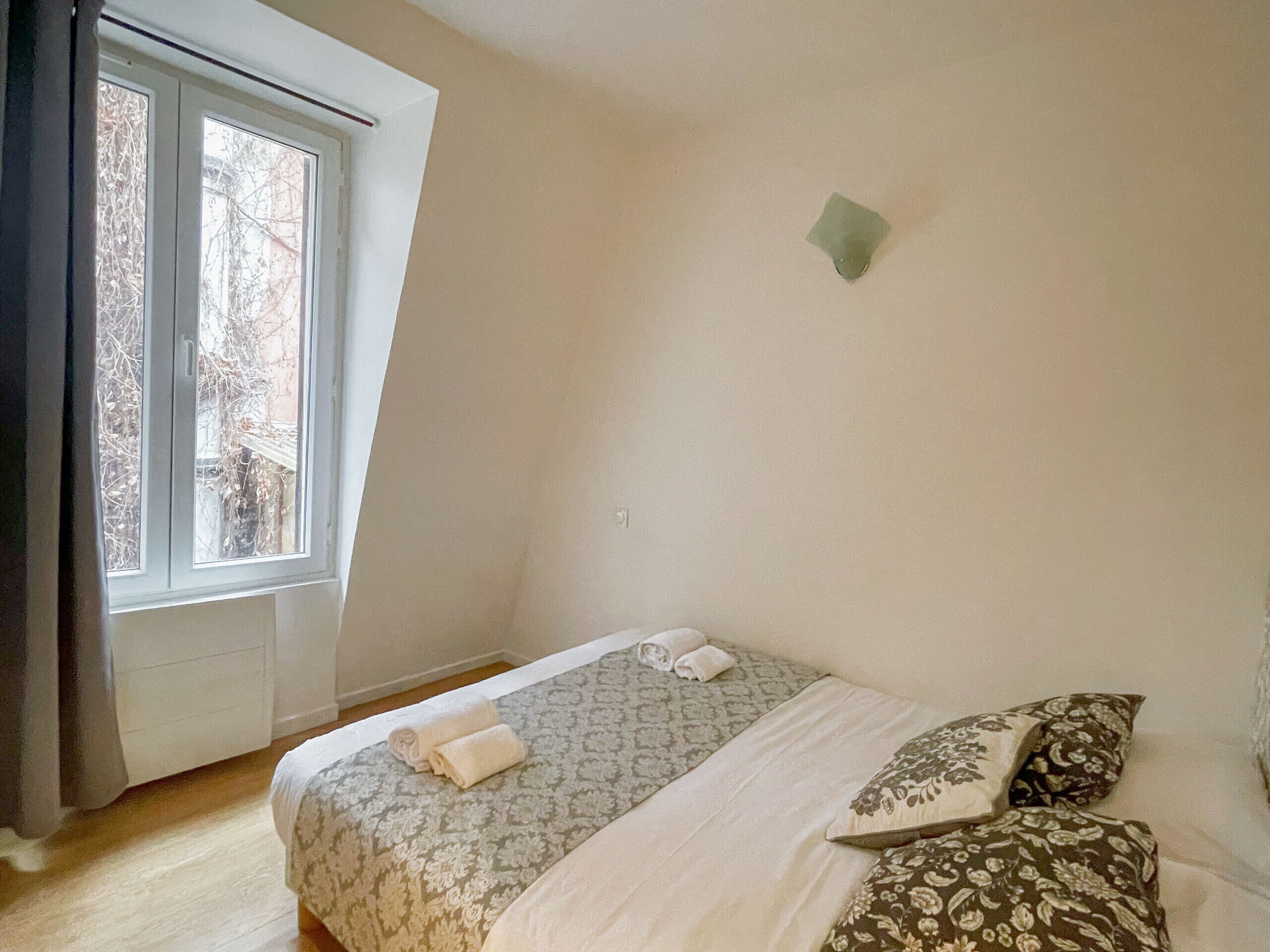 Ein Schlafzimmer mit einem Bett, Kissen, einem Fenster und einer Wandleuchte.