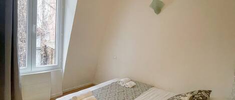 Ein Schlafzimmer mit einem Bett, Kissen, einem Fenster und einer Wandleuchte.