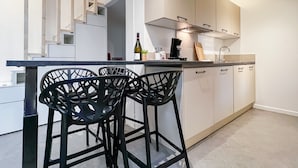 A modern kitchen with white cabinets, a black countertop, and two black bar stools. - Atypique sous château vieille ville (Annecy)