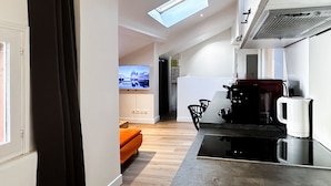 A compact kitchen with a modern design, a dining area with a sofa, and a television displaying a cityscape. - Atypique sous château vieille ville (Annecy)