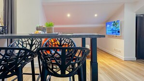 A modern dining area with a skylight, a flat-screen TV, and a wooden floor. - Atypique sous château vieille ville (Annecy)