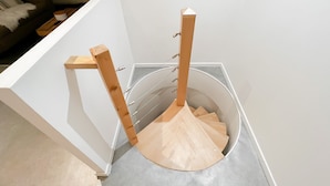 A modern, minimalist room with a white wall and a built-in wooden ladder leading to a circular platform. - Atypique sous château vieille ville (Annecy)