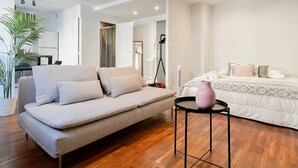 A modern living room with a sofa, a small table with a vase, and a bed with a patterned bedspread.