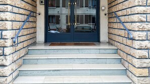A building entrance with a dark blue door, stone brick walls, and a set of stairs leading up to the door.