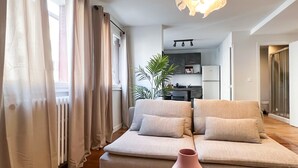 A modern living room with a beige sofa, a pink vase, and a dining area in the background.