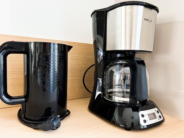 Una cafetera negra con un recipiente de acero inoxidable y un hervidor negro sobre una superficie de madera.