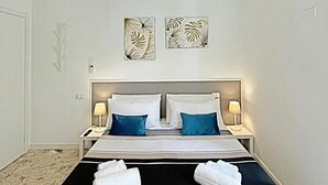 Quarto de hotel com cama, duas mesas de cabeceira, luminária pendente e decoração na parede.