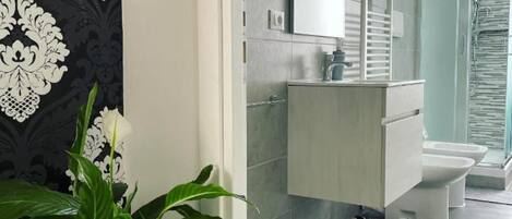 A modern bathroom with a grey tiled floor, a white sink, and a glass shower enclosure.