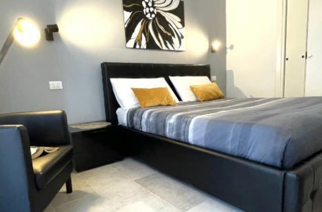 A bedroom with a bed, a nightstand, a chair, and a wall-mounted artwork.