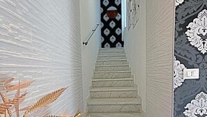 Uma escadaria com paredes brancas e papel de parede estampado, que leva a um quarto com porta de padrão preto e branco.