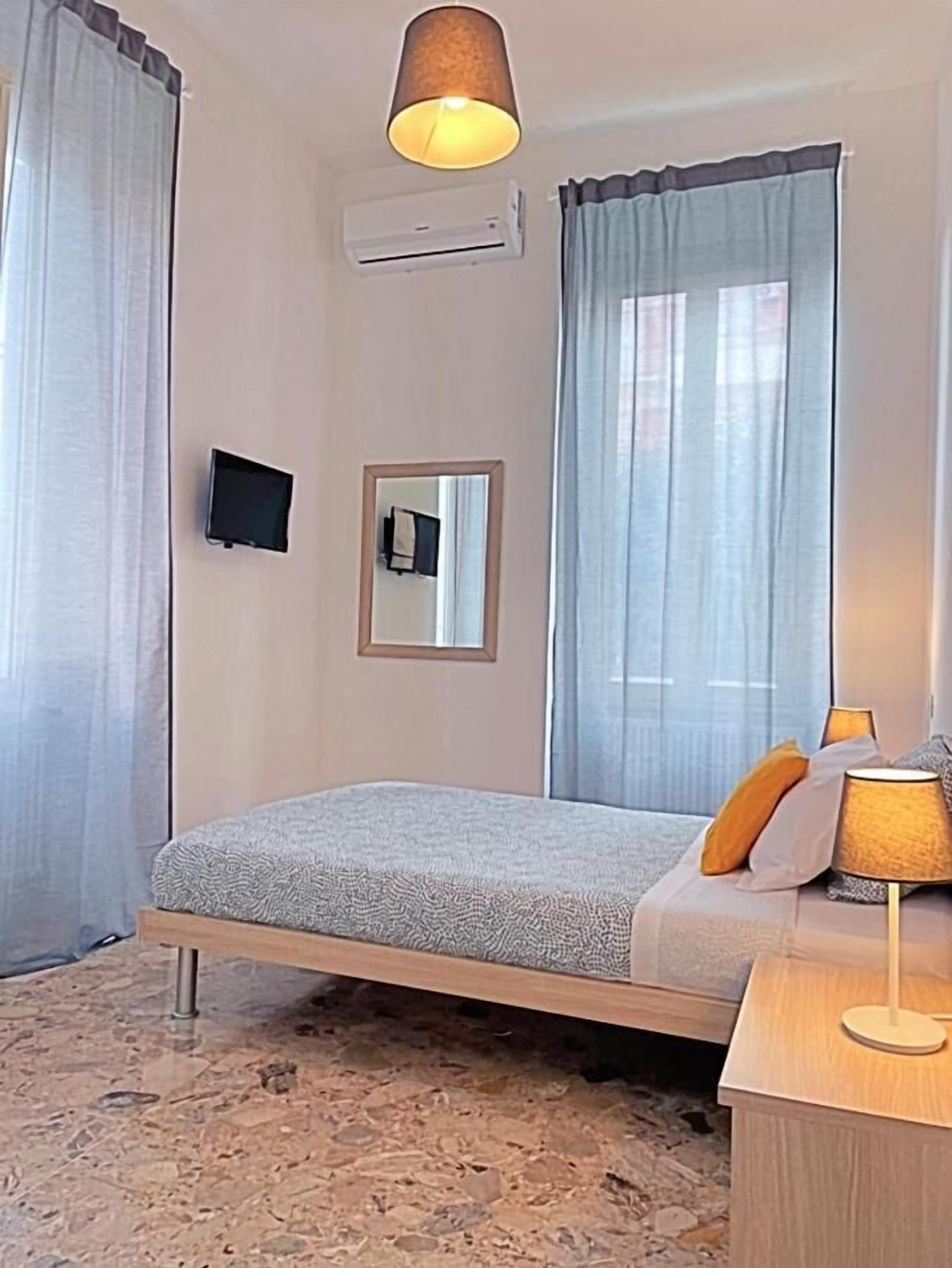 Ein Hotelzimmer mit Bett, Nachttisch mit Lampe, Fernseher, Spiegel und Klimaanlage.