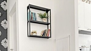 Uma sala de estar moderna com duas poltronas pretas, uma mesa redonda pequena com xícaras e pires, e uma estante acima.