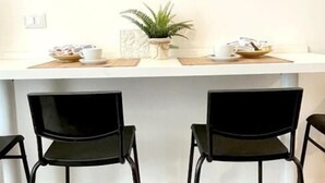 Uma área de recepção com um balcão branco, duas cadeiras pretas e três obras de arte emolduradas na parede.