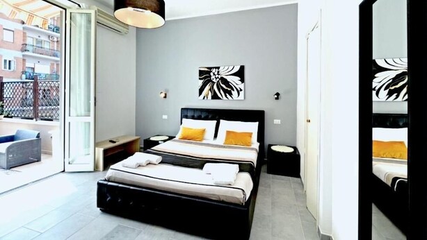 Um quarto moderno com uma cama grande, uma mesinha de cabeceira, um abajur e uma janela ampla.