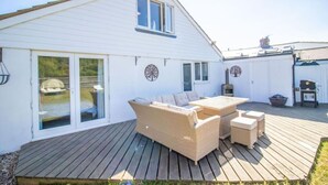 A white house with a deck, a wicker sofa, a table, and a grill.