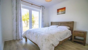 A bedroom with a wooden bed, a bedside table, and a view of the outdoors through a large window.