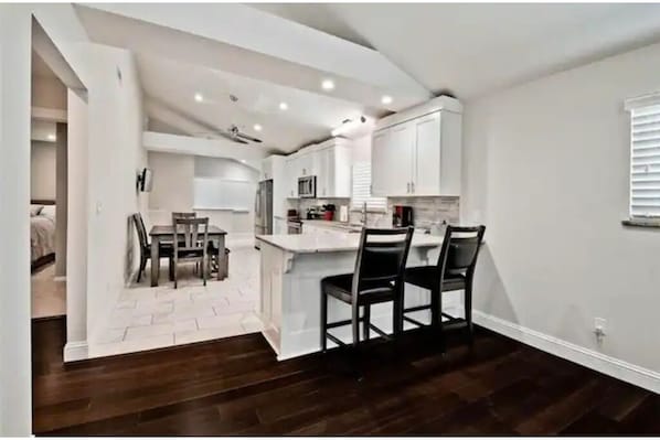 A modern kitchen with white cabinetry, a central island with chairs, and a dining area with a table and chairs.