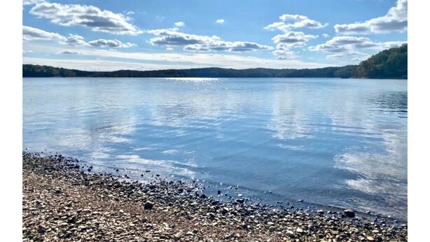 A calm lake with a pebbly shore and distant hills under a partly cloudy sky. - Lake View! Hot-Tub! Beaver Lake House! (Rogers)