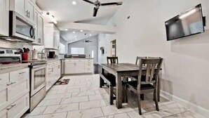 A modern kitchen with white cabinets, a built-in microwave, and a dining area with a wooden table and chairs. - Lake View! Hot-Tub! Beaver Lake House! (Rogers)
