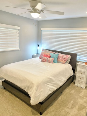 A bedroom with a bed, a ceiling fan, a nightstand with a lamp, and a dresser.