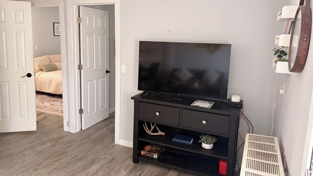 A room with a television on a black stand, a door leading to another room, and a white wall with a vent.