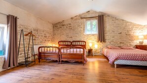 A bedroom with a stone wall, a wooden bed, a wooden chair, and a bedside table with a lamp. - Pet friendly home in Escles with WiFi (Escles)