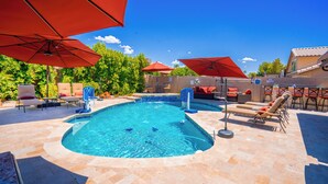 Ein Swimmingpool mit roten Sonnenschirmen, Liegestühlen und einer gefliesten Poolterrasse.