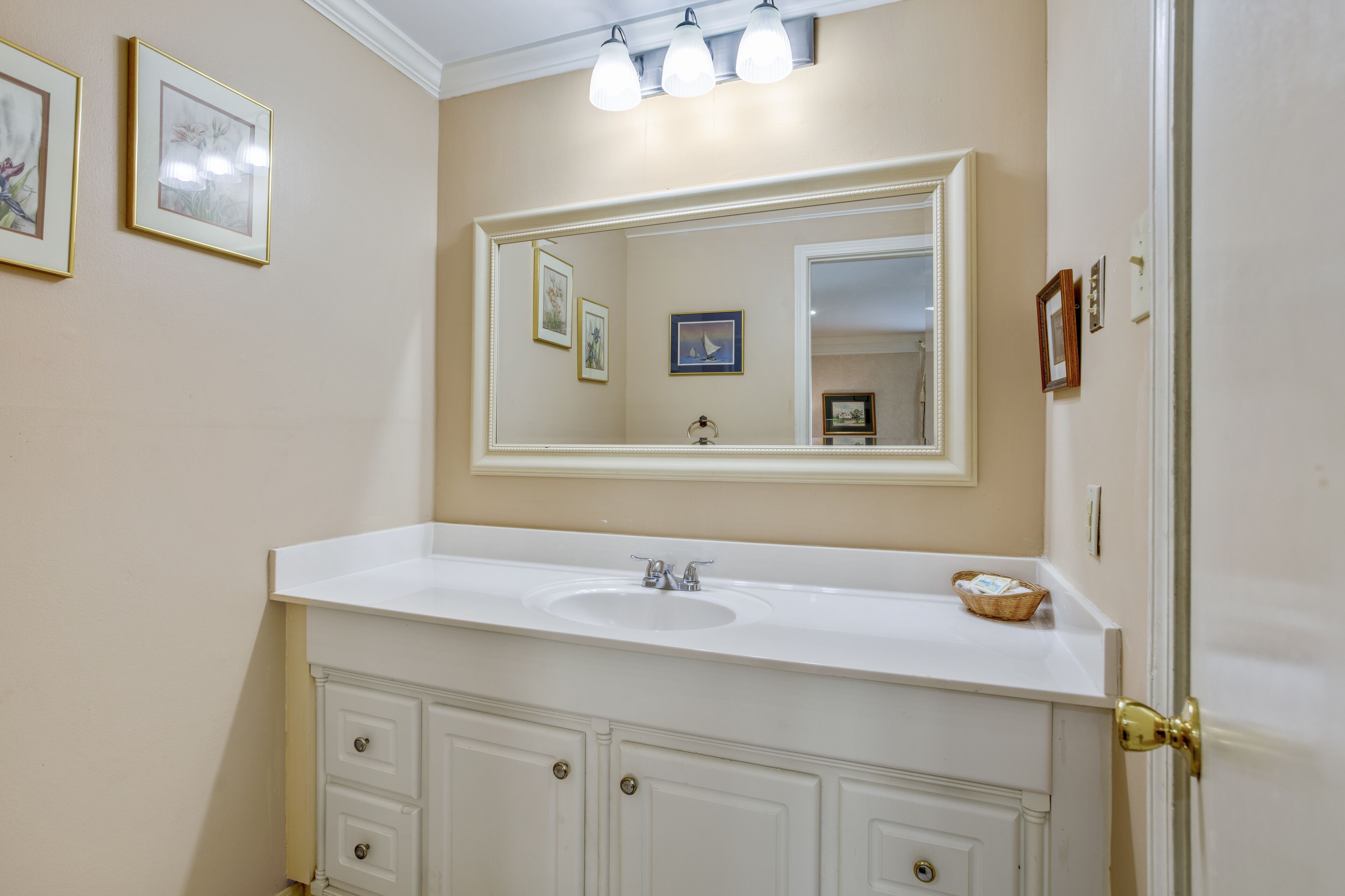 A bathroom with a white vanity, a large mirror, and framed pictures on the wall.