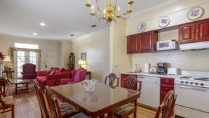 A dining area with a wooden table and chairs, a chandelier, and a kitchen with red cabinets and white appliances. - Edgewater Inn (Biloxi)