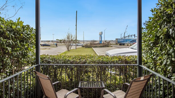 A balcony with chairs and a table, overlooking a parking area with a clear sky. - Edgewater Inn (Biloxi)