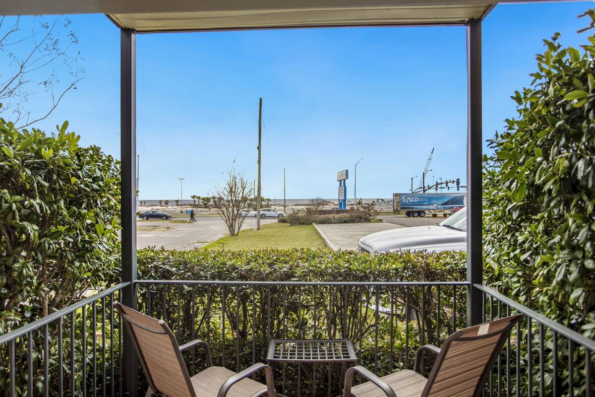 A balcony with chairs and a table, overlooking a parking area with a clear sky.