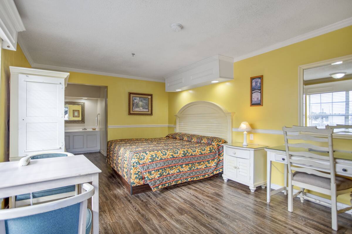 A bedroom with a bed, a desk, a chair, a dresser, and a mirror.
