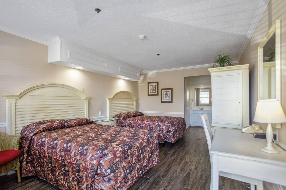 A bedroom with two beds, a desk, and a mirror.