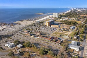 An aerial view of a coastal area with a large parking lot, several buildings, and a beach in the background.