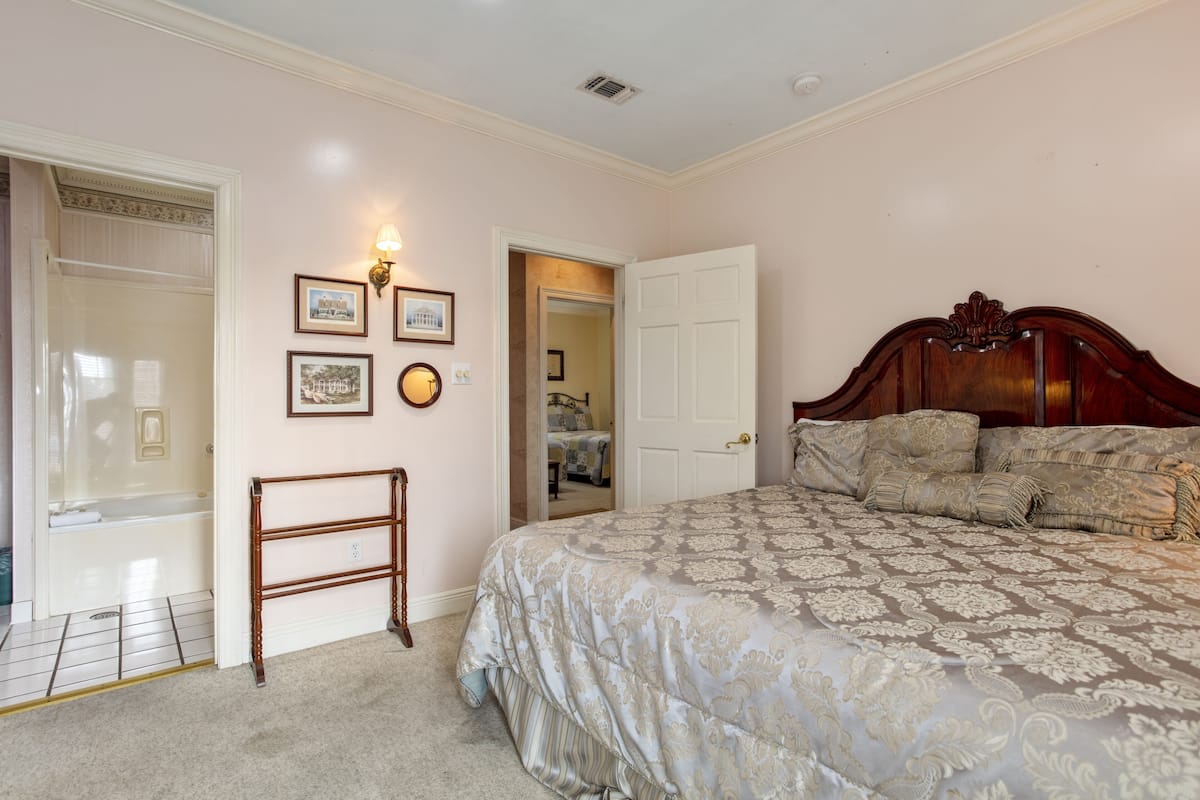 A bedroom with a large bed, a wooden headboard, a walk-in closet, and a mirror.