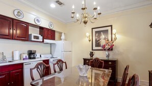 A dining area with a glass table, wooden chairs, a chandelier, a white refrigerator, a microwave, a stove, and a vase with flowers. - Edgewater Inn (Biloxi)