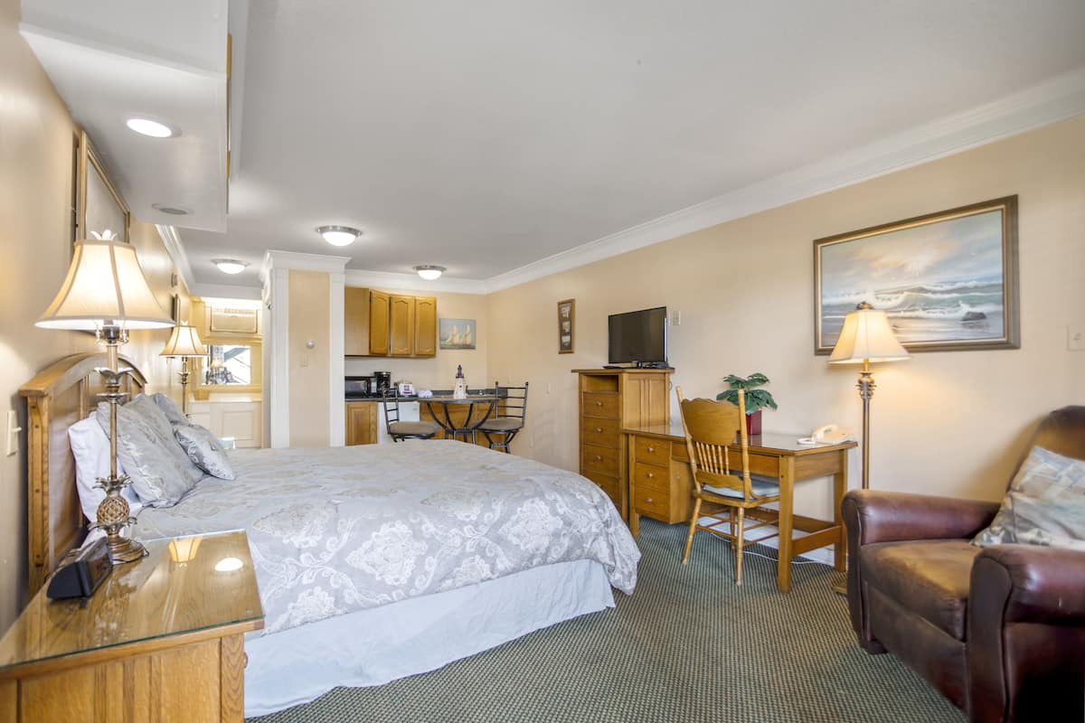 A hotel room with a large bed, a desk, a chair, a television, and a painting on the wall.