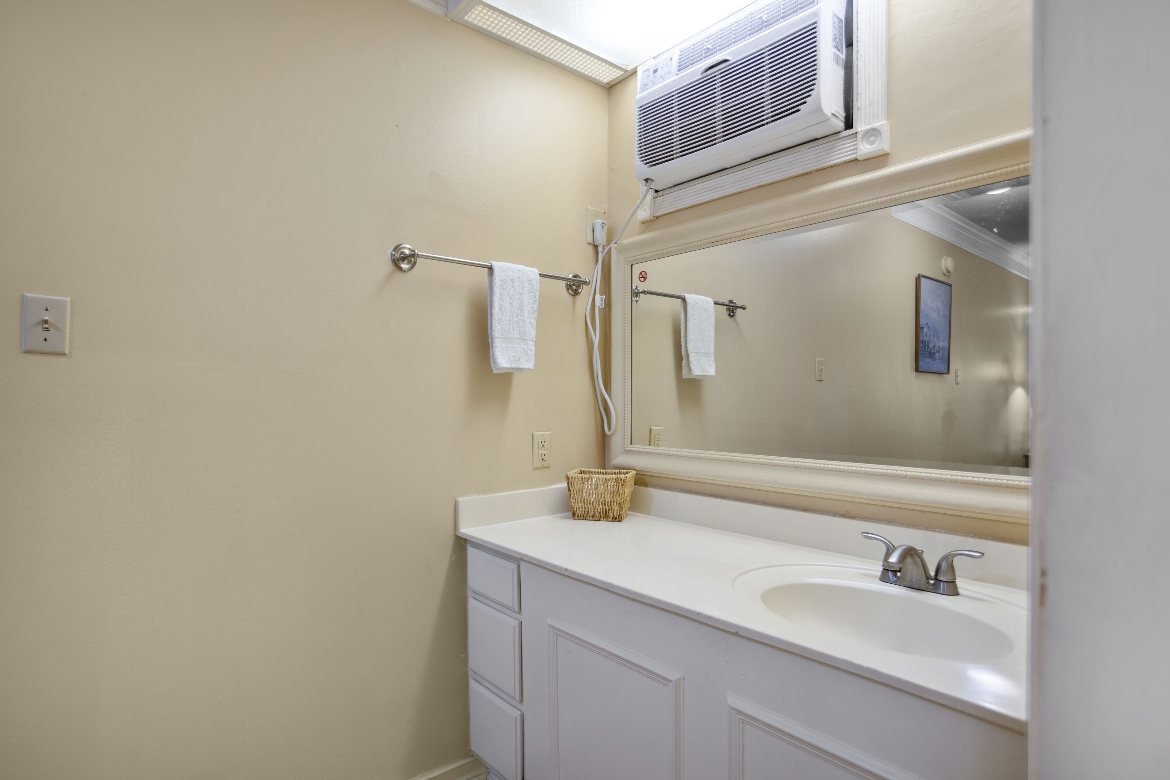 A bathroom with a white sink, a mirror, a towel rack, and a wall-mounted air conditioner.