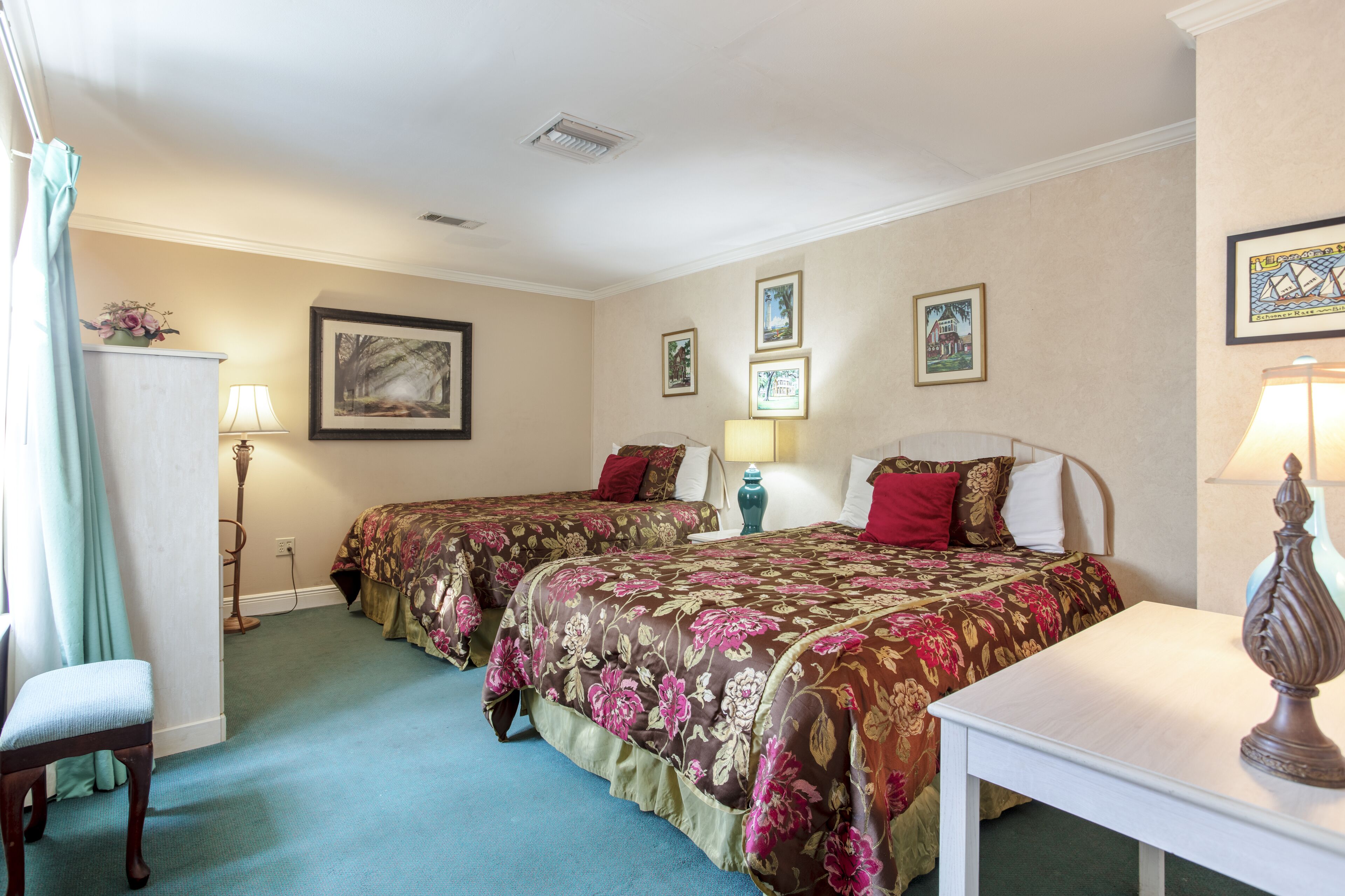 A hotel room with two beds, a desk, a chair, and a lamp.