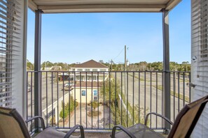 A balcony with a view of a building, a parking lot, and a clear sky.