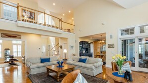 A spacious living room with a high ceiling, a staircase leading to an upper level, and a dining area with a table and chairs. - Beautiful New Seabury Home in Mashpee (Mashpee)