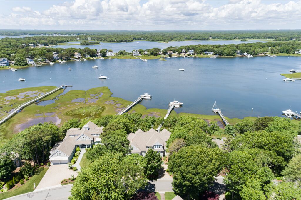 A lakeside property with a dock, boats, and a large house surrounded by trees.