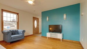 Una sala de estar con pared azul, piso de madera, sofá azul, mueble de televisión blanco y puerta de madera con ventanal.