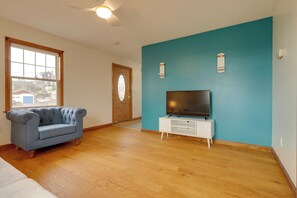 Ein Wohnzimmer mit blauer Wand, Holzboden, einem blauen Sofa, einer weißen TV-Konsole und einer Holztür mit Glasfenster.