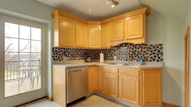 Una cocina con armarios de madera, lavavajillas, salpicadero de azulejos y ventana con vistas al exterior.