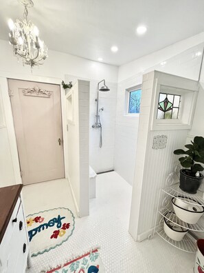 Bathroom features a shower with handheld showerhead, white tiled floor, and stained glass window.