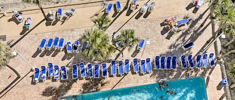 An aerial view of a beach with rows of blue lounge chairs and a swimming pool.