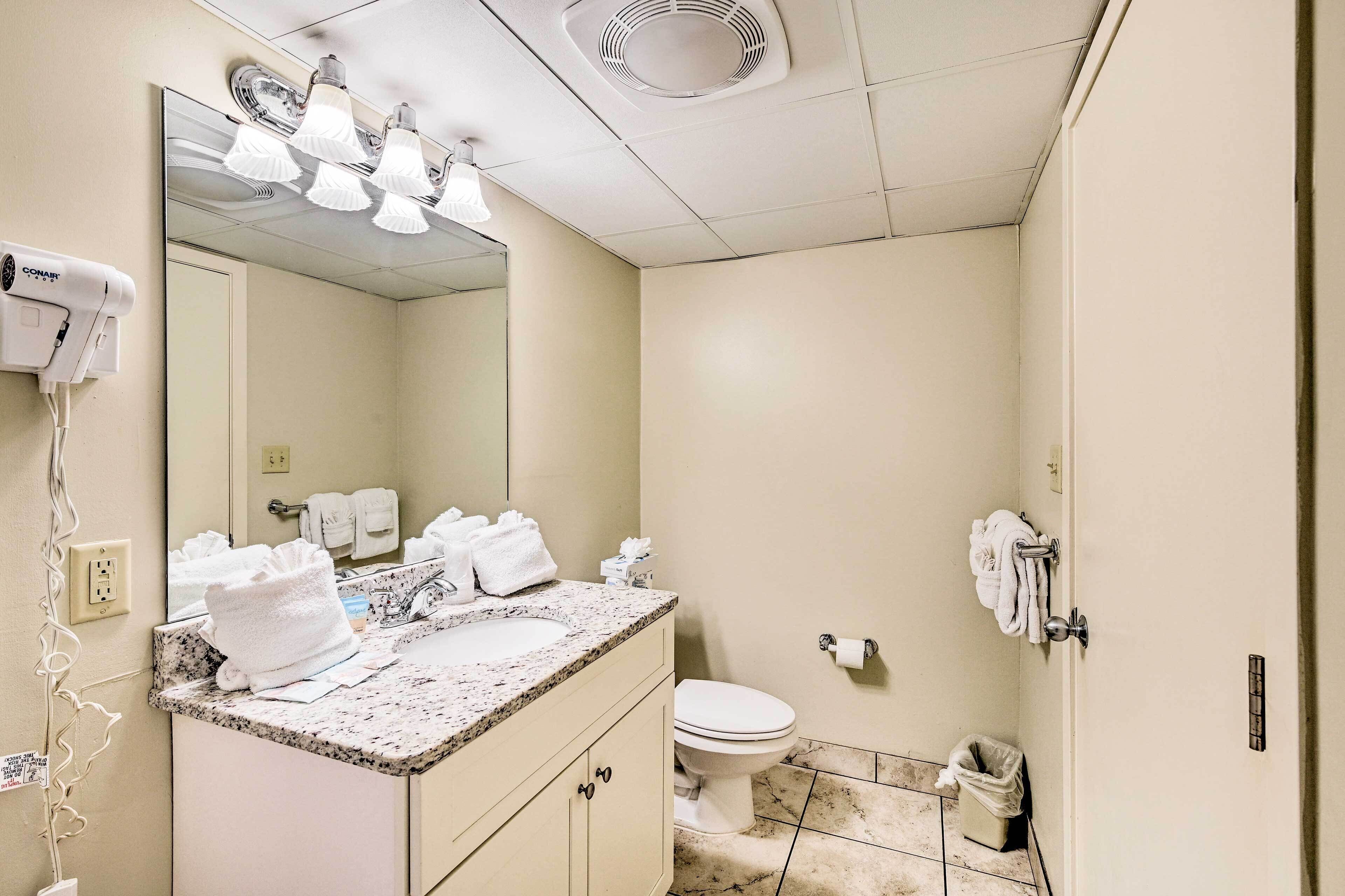 A bathroom with a sink, mirror, and toilet. There are towels and a trash can visible.